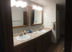 a bathroom with two sinks, mirrors and lights on the wall above them is shown