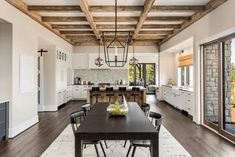 a dining room table and chairs in front of an open kitchen with wood beams on the ceiling