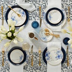 the table is set with blue and white plates, silverware, and gold utensils