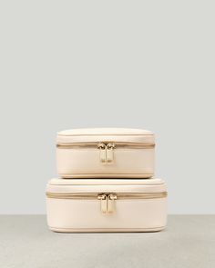 two white suitcases stacked on top of each other with gold handles and zippers