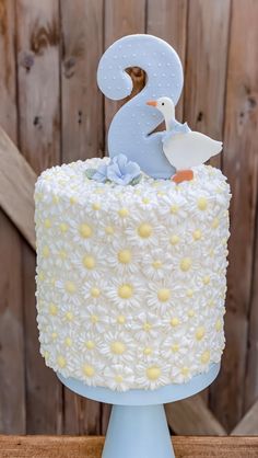 a white cake with yellow flowers and a blue bird on top is sitting on a wooden table