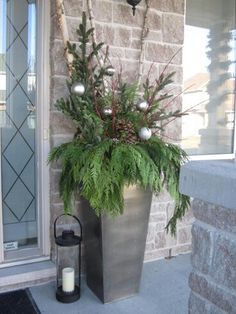 a large metal planter filled with greenery next to a brick wall and lantern