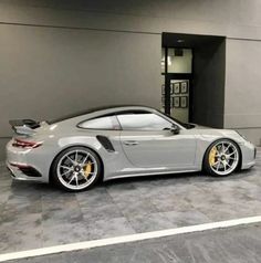 a grey sports car parked in front of a gray building with yellow wheels and rims