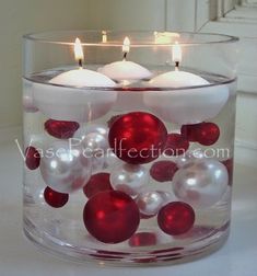 two candles are in a glass bowl with red and white ornaments on the bottom one candle is lit