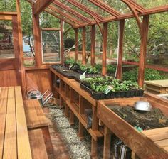 the inside of a wooden greenhouse with many plants growing in pots and on benches next to it