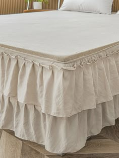 a white bed with ruffled bedskirt and pillows on top of the headboard