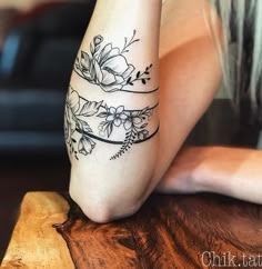 a woman's legs with flowers and vines tattooed on her left leg, sitting on a wooden table