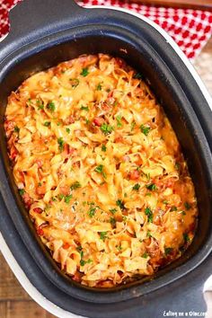 a casserole dish with noodles and meat in it on a wooden table next to a red checkered napkin