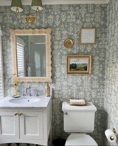 a white toilet sitting next to a sink in a bathroom under a mirror and framed pictures