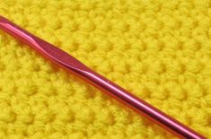 a pink toothbrush sitting on top of a yellow crocheted surface next to a red handle