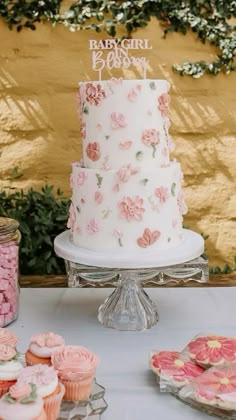 a white cake with pink flowers on it and cupcakes sitting next to it