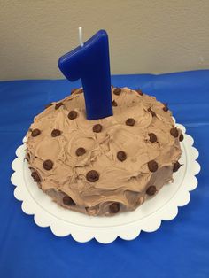 a chocolate cake with a candle in the shape of number one on a blue tablecloth