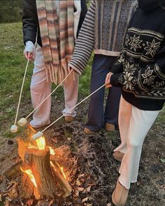 four people standing around a campfire with stick and balls on it's sticks