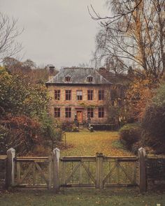 an old stone house surrounded by trees and bushes in the fall with leaves on the ground