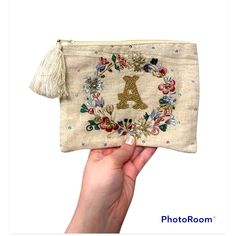 a hand holding an embroidered pouch with the letter a on it and flowers around it