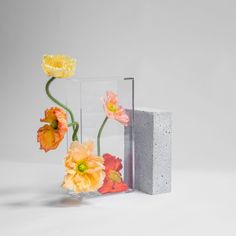 three flowers are placed in a vase next to a concrete block on a white surface