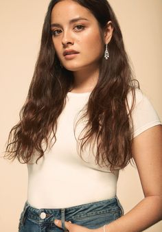 a woman with long brown hair wearing a white shirt and blue jeans is looking at the camera