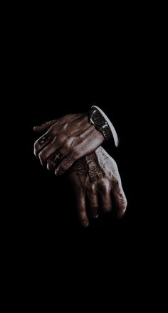 a person's hand with a wrist watch on it in the dark, against a black background