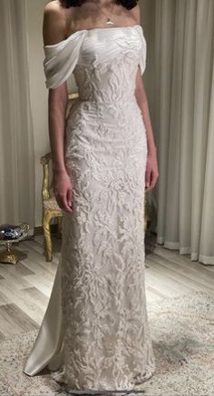 a woman standing in front of a window wearing a white dress with an off the shoulder design