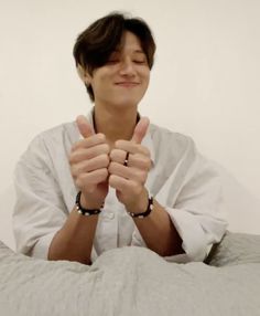 a woman sitting on top of a bed with her hands in the air and smiling