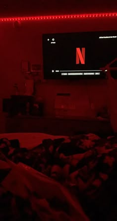 a bed in a room with red lights on the wall and a television mounted above it