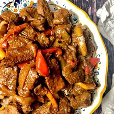 a plate full of beef and peppers on a table with napkins next to it