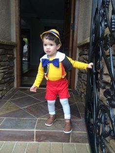 a little boy dressed up as mickey mouse in front of a gate with his hand on the door handle