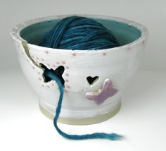 a ball of yarn in a white bowl with hearts on the side and blue string