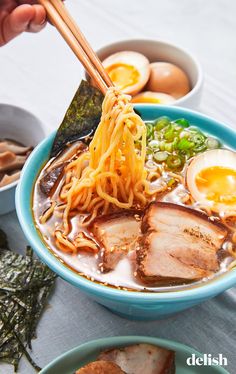 someone holding chopsticks over a bowl of ramen with meat and eggs in it