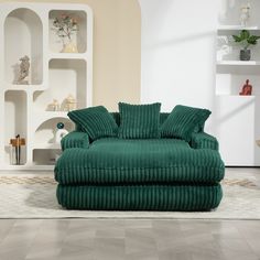 a large green couch sitting on top of a white floor next to a shelf filled with vases