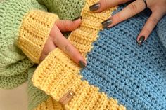 a woman's hands holding onto a crocheted sweater with two different colors