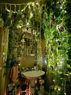 a bathroom filled with lots of green plants and lights hanging from the ceiling next to a sink