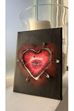 a painting on a shelf with a candle and vase in the background that has a red heart painted on it