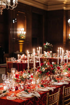 a long table is set with red and white flowers, candles, and place settings