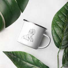 a white coffee mug with a drawing of a man on it next to green leaves