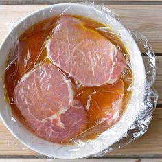 two pieces of meat wrapped in plastic sitting on top of a wooden table