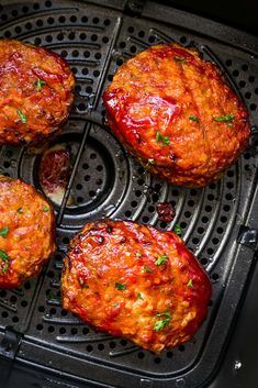 four hamburger patties cooking in an air fryer with ketchup and parsley