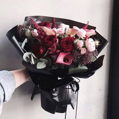 a woman holding a bouquet of red and pink flowers in her hand, against a white wall