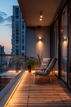 a balcony with two chairs and a plant on the floor next to glass doors at night