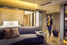 a woman is walking through a hotel room with her luggage in front of the bed