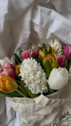 a bouquet of tulips and other flowers in a white bag on a bed