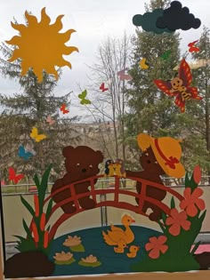 a window decorated with paper cut outs and teddy bears on a bridge over a pond