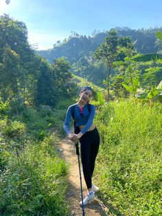 a woman standing on top of a dirt road next to lush green grass and trees