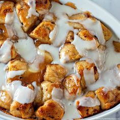 a white bowl filled with cinnamon rolls covered in icing and sauce on top of a table