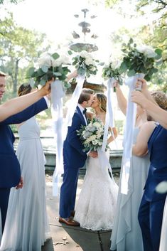 a bride and groom kiss as their bridal party takes place in front of them