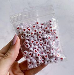 a bag of white and red heart shaped beads in someone's hand with their fingers