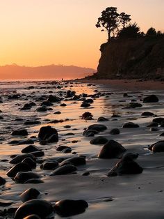 the sun is setting at the beach with rocks in the water and people walking on the shore