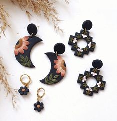 three pairs of earrings with flowers on them sitting next to some dried grass and branches