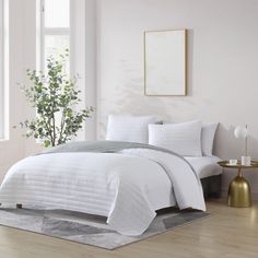 a bed with white comforters and pillows in a room next to a potted plant