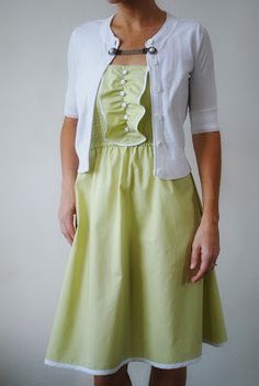 a woman standing in front of a white wall wearing a green dress and cardigan